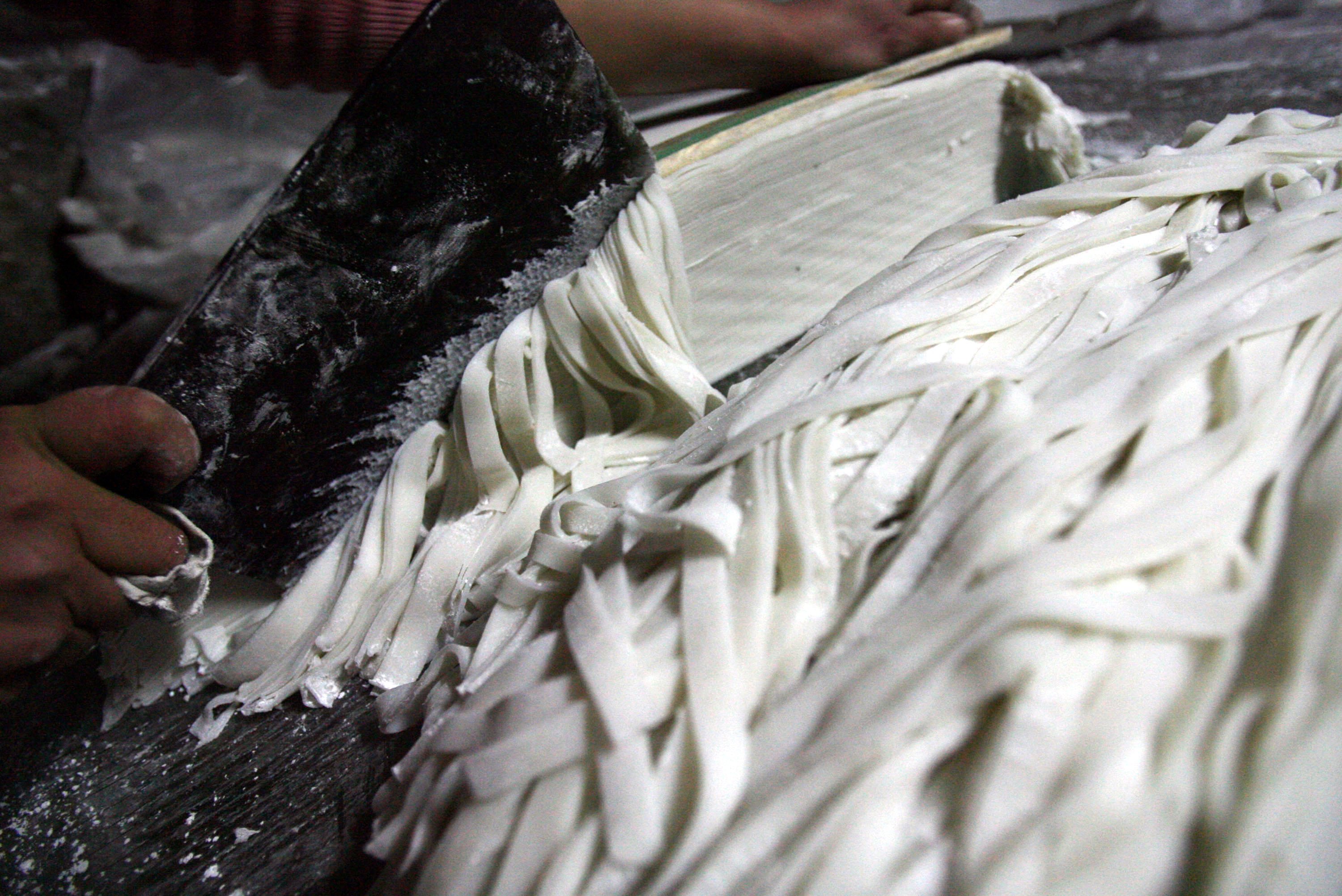 CHONGQING, CHINA - JANUARY 25: (CHINA OUT) A worker cuts rice noodles at a noodle workshop in Wansheng District on January 25, 2007 in Chongqing Municipality, China. Rice noodles are made from rice, and come in a variety of sizes. Cities from southwest of China as Chongqing, Chengdu and Guilin are famous for its rice noodle snacks, particularly spicy and sour noodle. (Photo by China Photos/Getty Images)