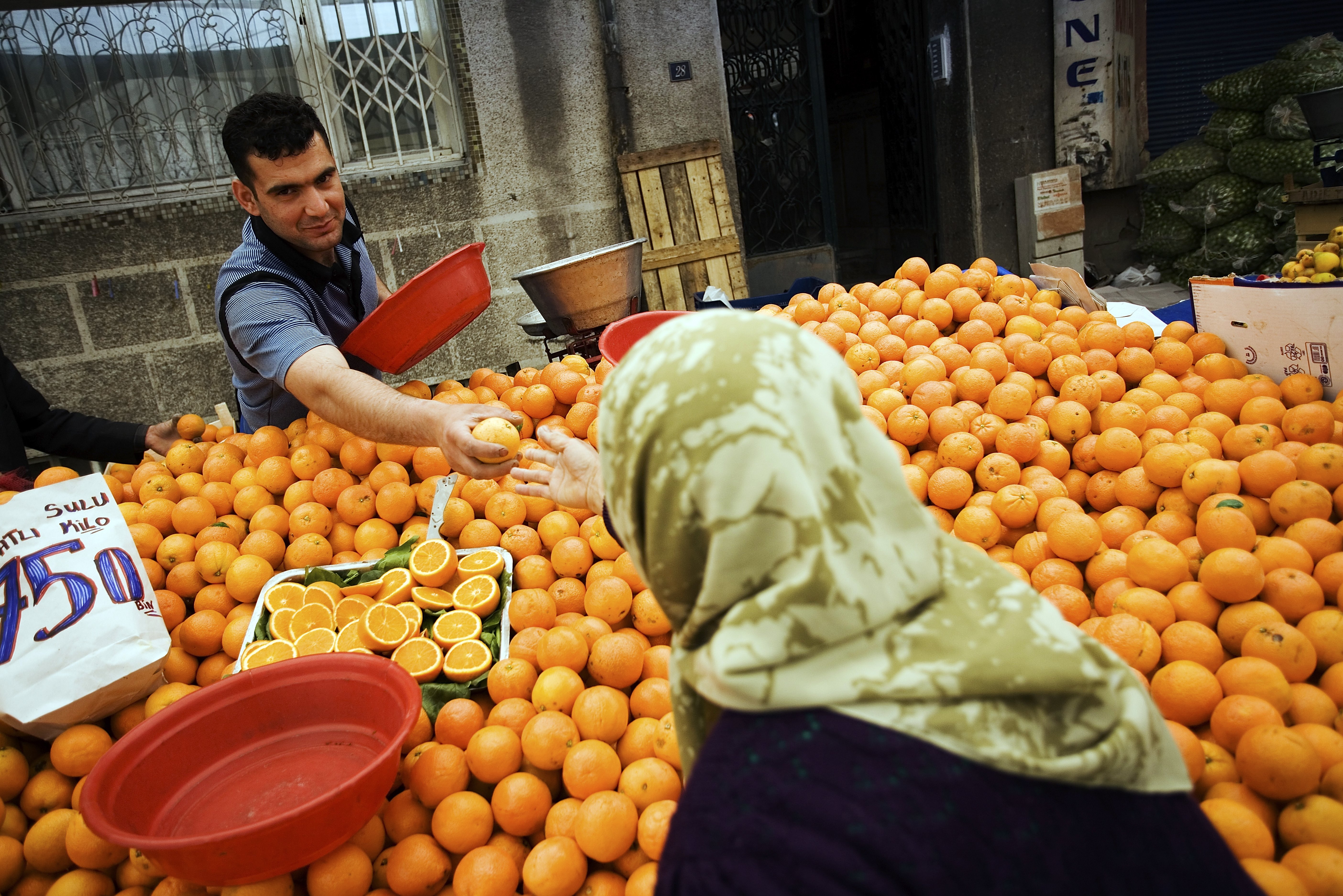 ISTANBUL, TURKEY- MAY 14: A fruit seller offers oranges to a scarfed woman on the weekly market in the district Tarlabasi on May 14, 2006 in Istanbul, Turkey.  Tarlabasõ is a neighbourhood in the Beyoglu district stretching from Taksim Square and Talimhane in the north to Tepebasõ in the south. It is bordered on the east side by the four-lane Tarlabasõ Caddesi and by Dolapdere Caddesi on the west. Historically, Tarlabasõ was home to a large Greek population. In the 1990s, large numbers of Kurdish immigrants from eastern Turkey moved into Tarlabasõ mixing in with the local Roma population. More recently, it has become the home to many migrants from neighbouring countries and Africa. The Turkish metropolis on the Bosphorus, in the past capital various empires, like the Roman, Byzantine and Ottoman Empire, is designated by the European Union as The European Capital of Culture for a period of 2010 during which it is given a chance to showcase its cultural life and cultural development.  (Photo by Carsten Koall/Getty Images)