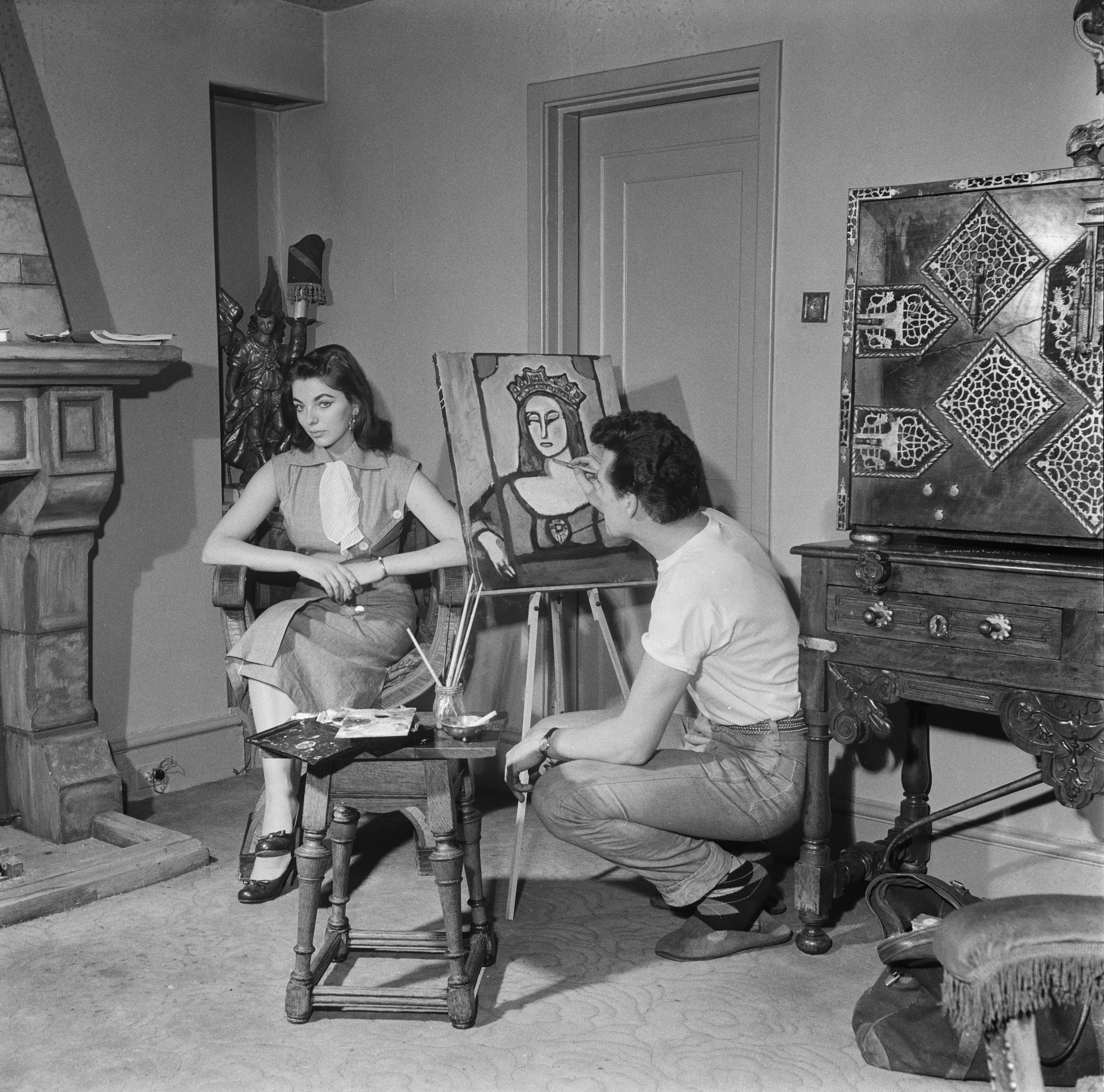 Actor Maxwell Reed paints a portrait of his wife, actress Joan Collins, wearing a crown, at their flat in Hanover Square, London, 8th May 1953. (Photo by John Pratt/Keystone Features/Hulton Archive/Getty Images)