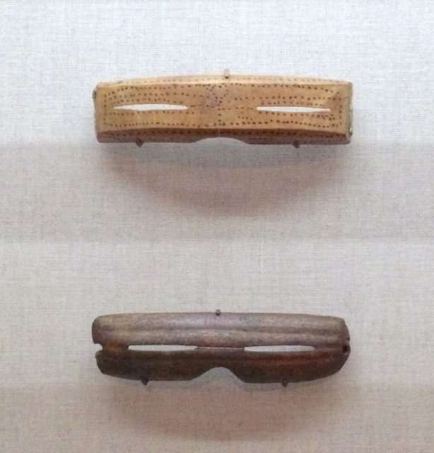 Inuit Snow goggles from Alaska. Made from carved wood, 1880-1890CE (top) and Caribou antler 1000-1800 CE (bottom). Author: Jaredzimmerman (WMF) – CC BY-SA 4.0
