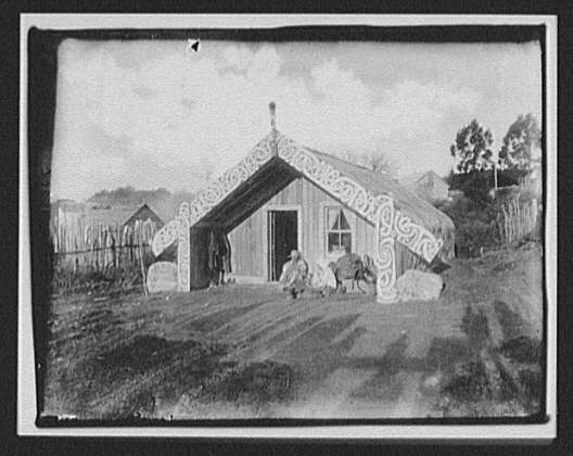 Man, woman and baby in front of ornamented Māori house, 1895