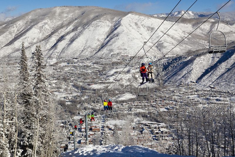 Skiers and snowboarders ride up the iconic Lift 1A on Aspen Mountain with downtown Aspen in the background. – Author: AspenSkiingCompany – CC BY-SA 3.0