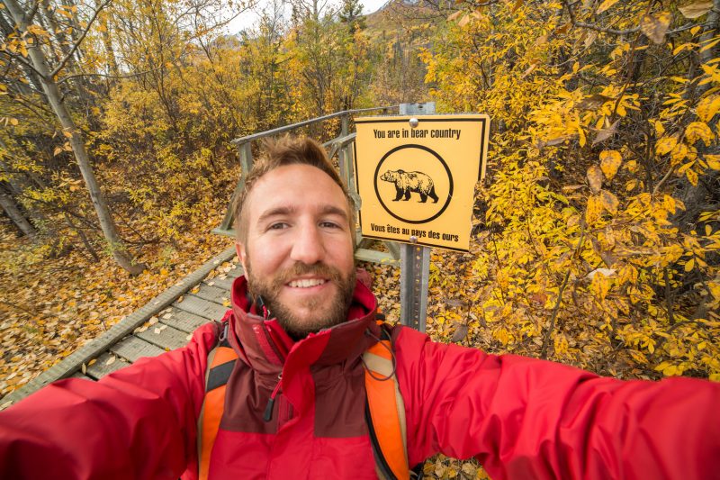Hiking in autumn in Canada. Taking a selfie portrait near the warning bear sign…