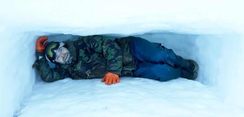 A survival specialist lying in the sleeping section of a shelter carved out of the snow