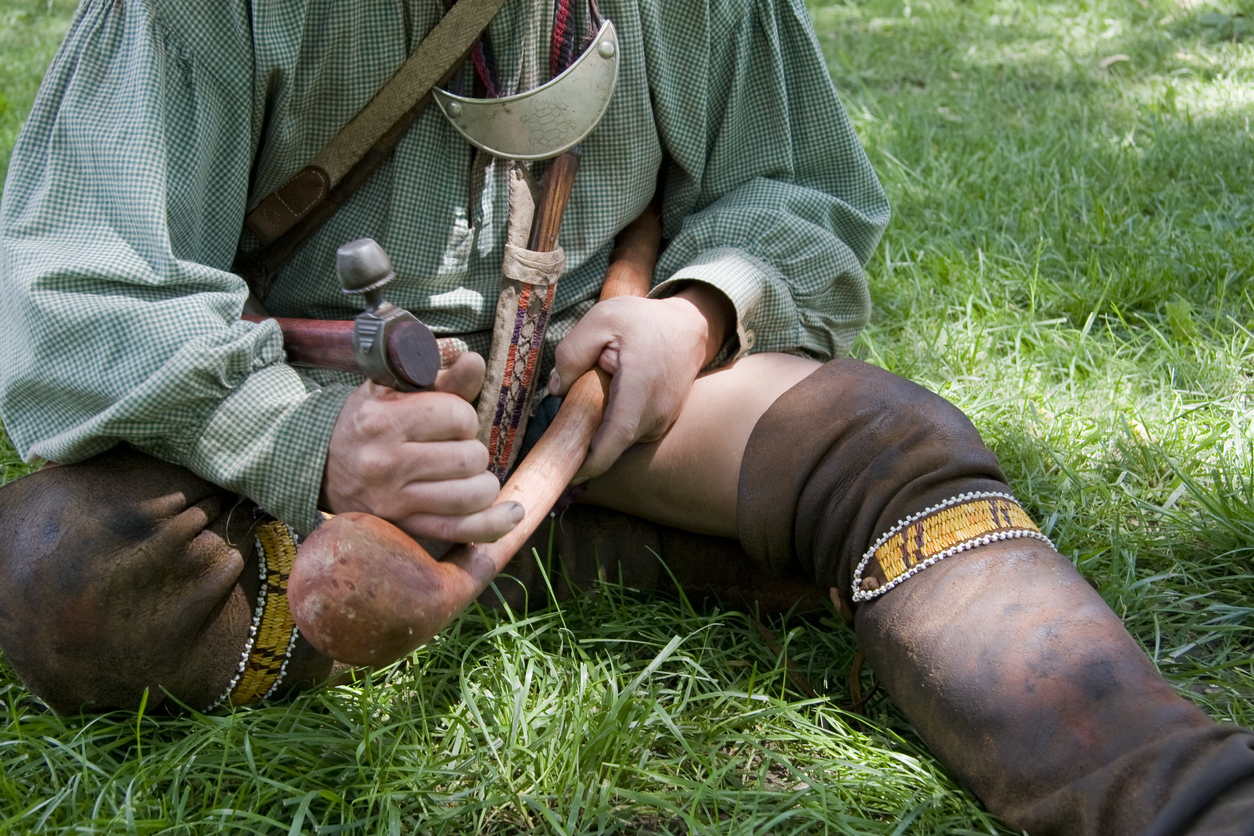 A reenactor portraying an Iroquois Indian from the New York Senaca tribe.  He is using his Tomahawk to carve his war club.  The war club was used as the primary weapon by the Iroquois during the French and Indian war.