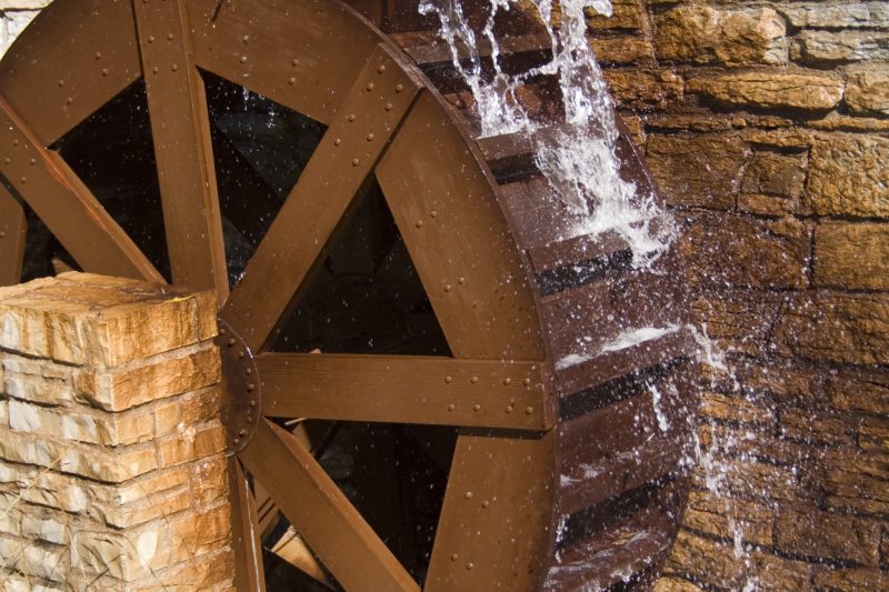 A wooden water wheel is driven by the momentum of the moving water