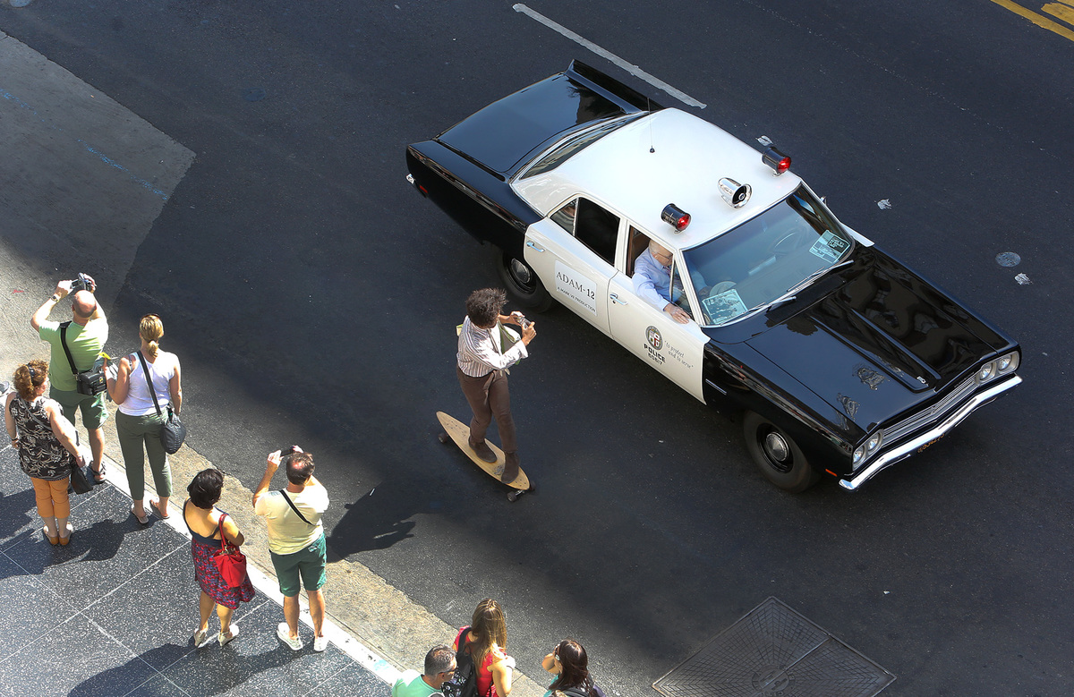 A skateboarder photographs a 1972 AMC Matador vehicle as it travels along Hollywood Blvd. in Hollyw