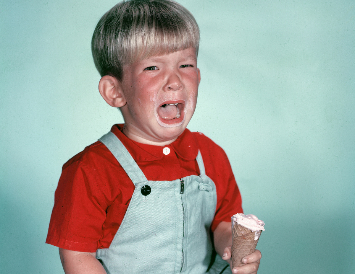 Studio portrait of a young boy crying as he holds a melting ice cream cone, circa 1962.