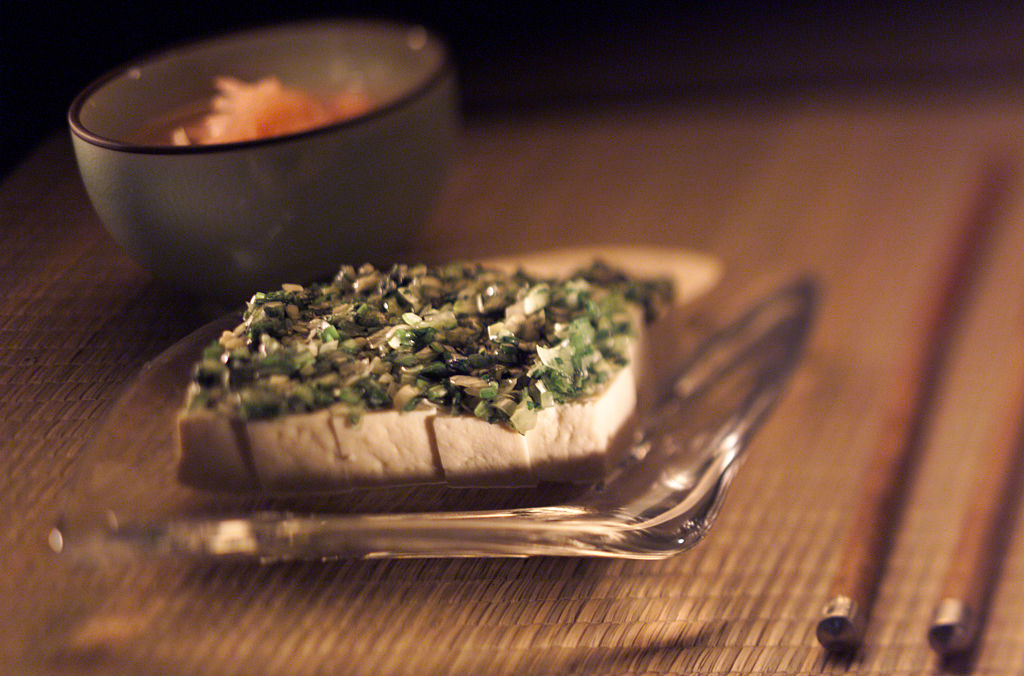 A tofu meal sits on a plate and is toppped with green onions