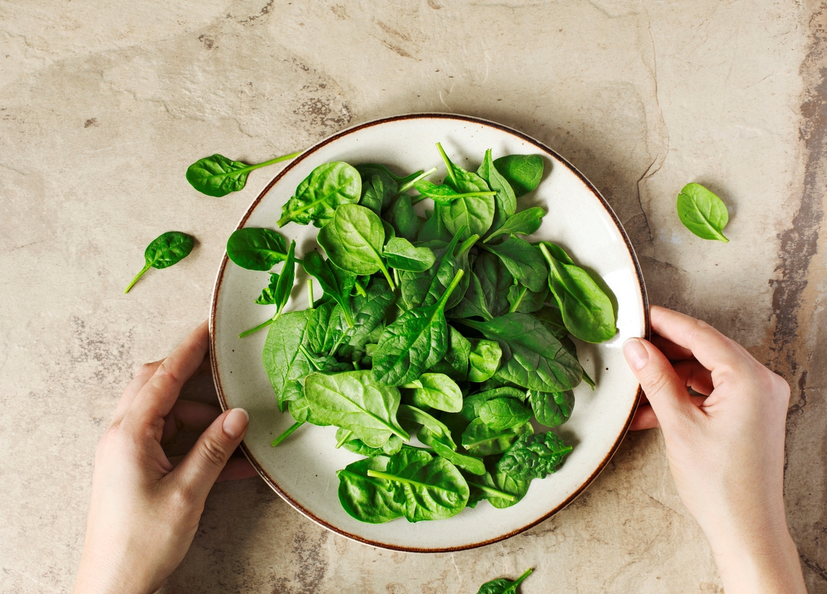 Woman sets a plate full of spinach down on a table.