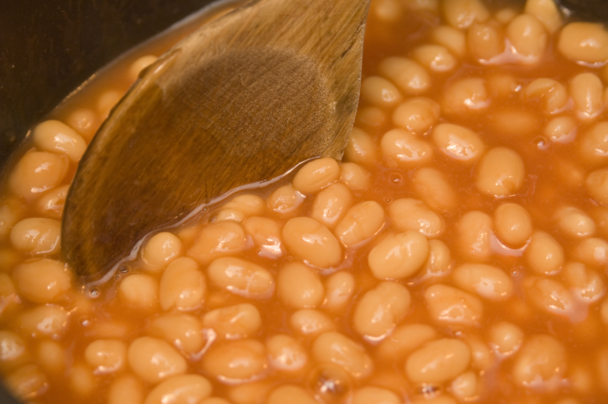 A wooden spoon mixes a pot of baked beans.