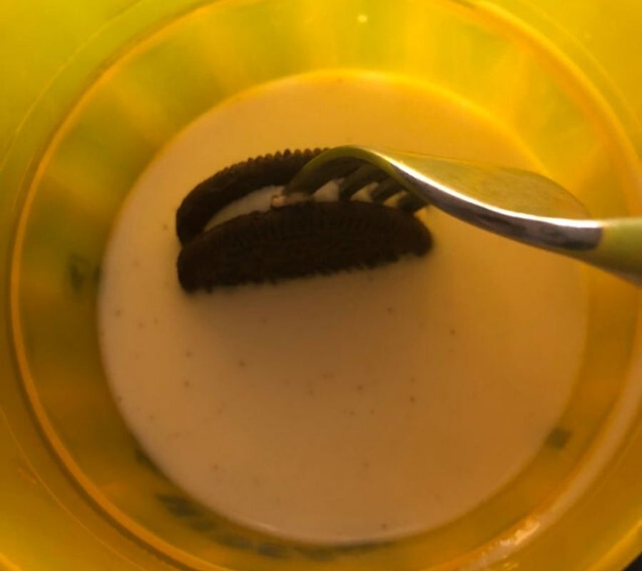 a fork stuck into the middle of an oreo cookie being dipped in milk