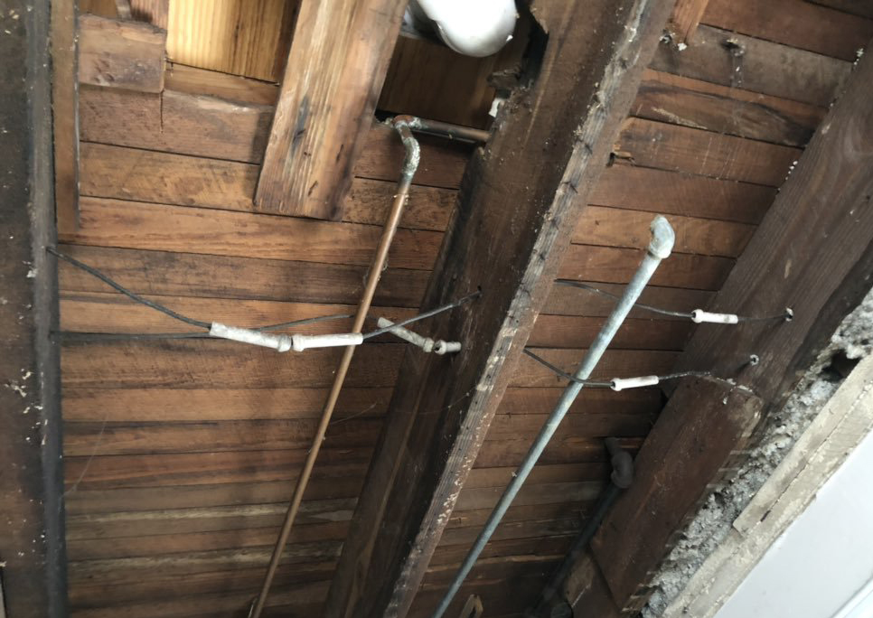 Knob and wire tubing lines a wooden ceiling in the basement.