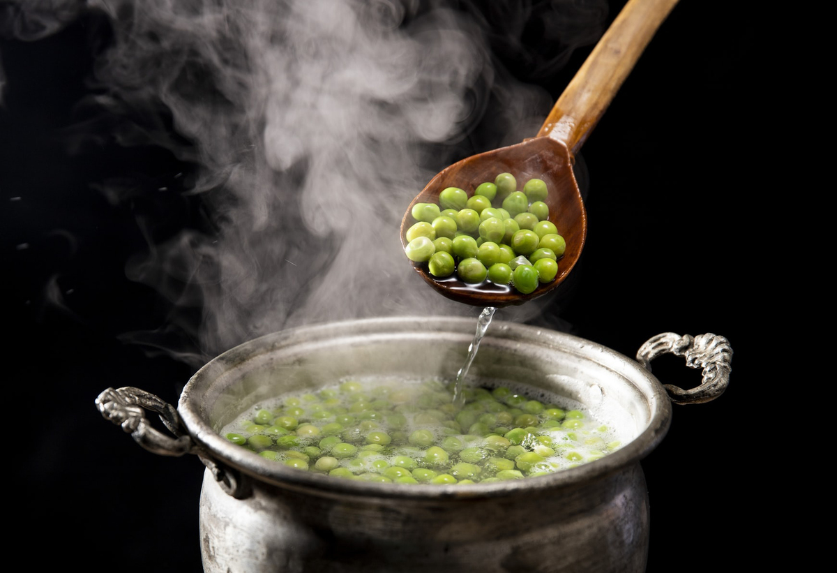Cooked peas are dished out of a pot with a wooden spoon.