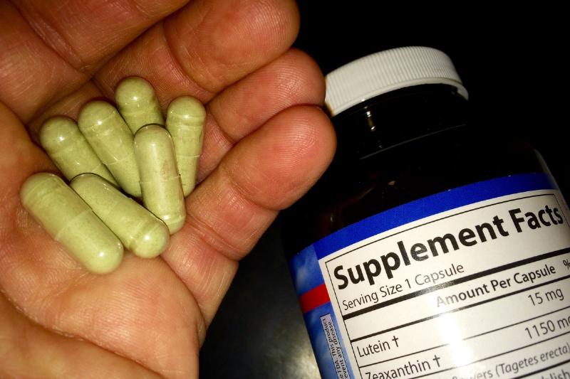 A man holds marigold herbal supplement capsules with the bottle nearby.