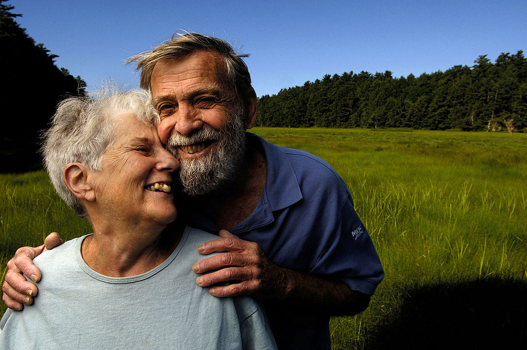 An elderly couple smiles and pose close together.