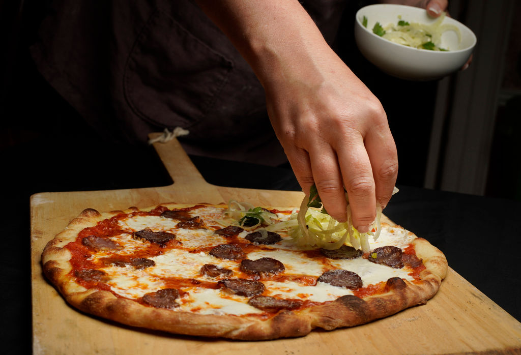 someone putting toppings on a pizza