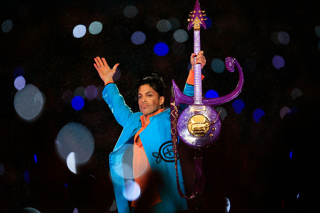 Prince raises his arms and his guitar while performing at the Super Bowl.