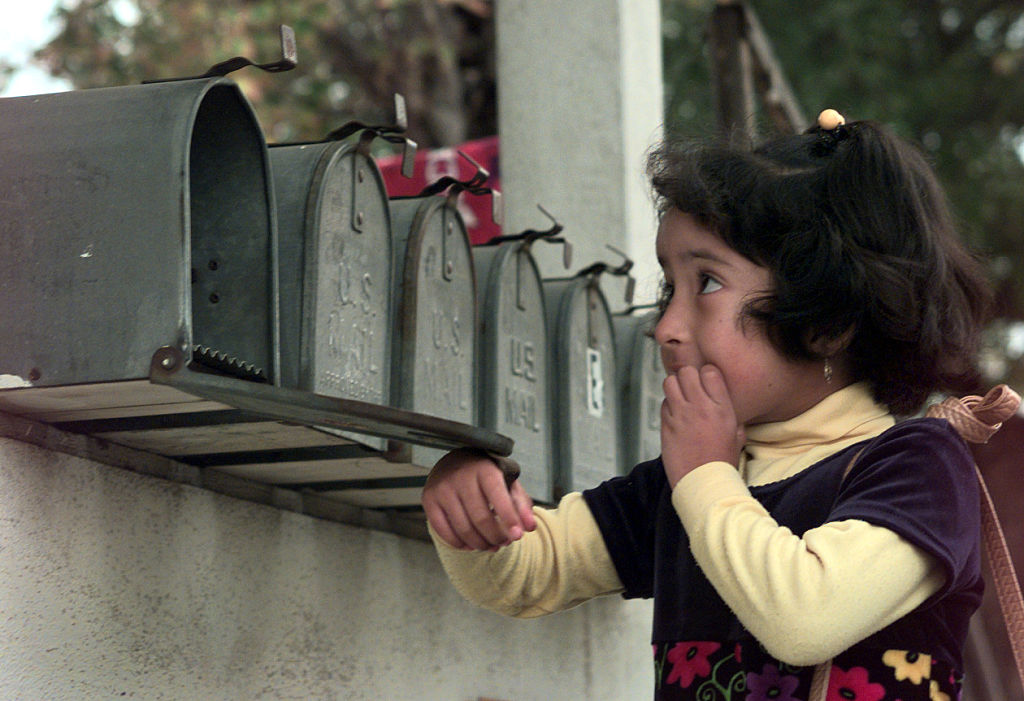 A young girl checks a mailbox that's one of several identical mailboxes in a row.