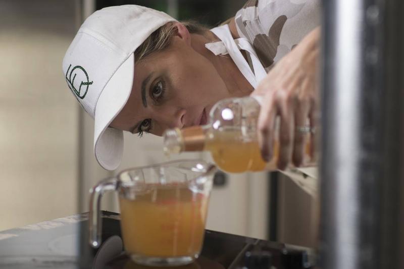 A woman pours apple cider vinegar into elderberry syrup.