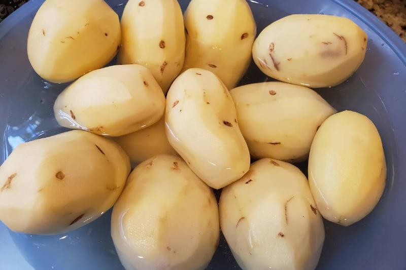 Peeled potatoes soak in water in a blue bowl.