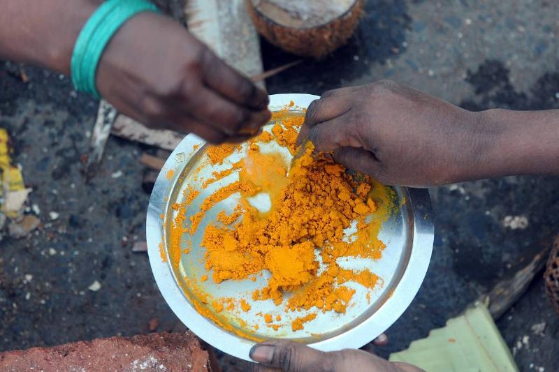 Women pick up powdered turmeric from a plate.