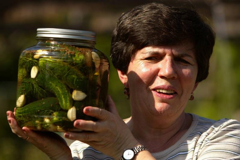 A woman holds up a jar of dill pickles.