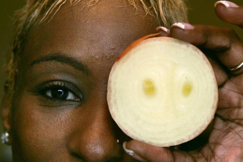 A woman holds up a white onion in front of her eye.