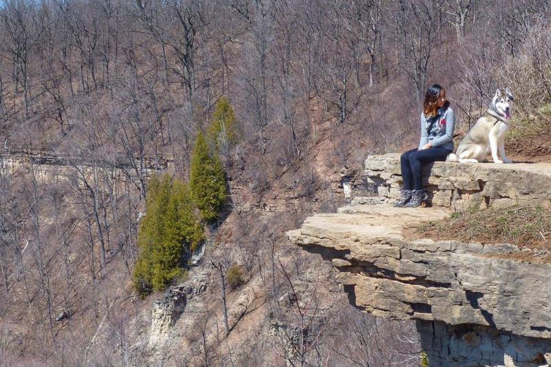 A woman and her dog sit on a rock on a cliff.