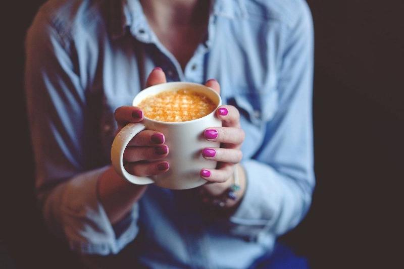 A woman in a blue shirt holds a latte in a mug.