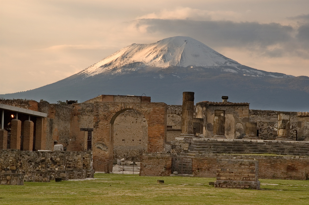 The sun begins to set on the snow capped Mount Vesuvius still overlooking Temple of Jupiter standing in the forum of Pompeii