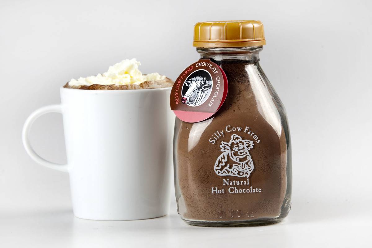 A mug of hot chocolate stands next to the cocoa mixture and lactose-free milks.