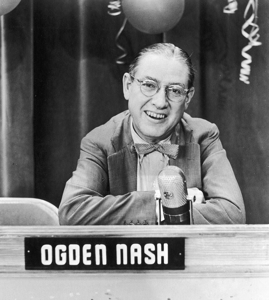 circa 1955: American poet and lyricist Ogden Nash, wearing eyeglasses and a bow tie, smiles while sitting on a television quiz show panel, 1950s. 