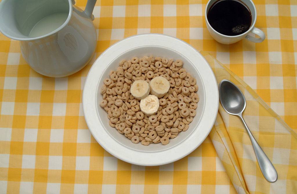 View of a table setting with a bowl of breakfast cereal (and banana slices), a cup of coffee, and a pitcher of milk