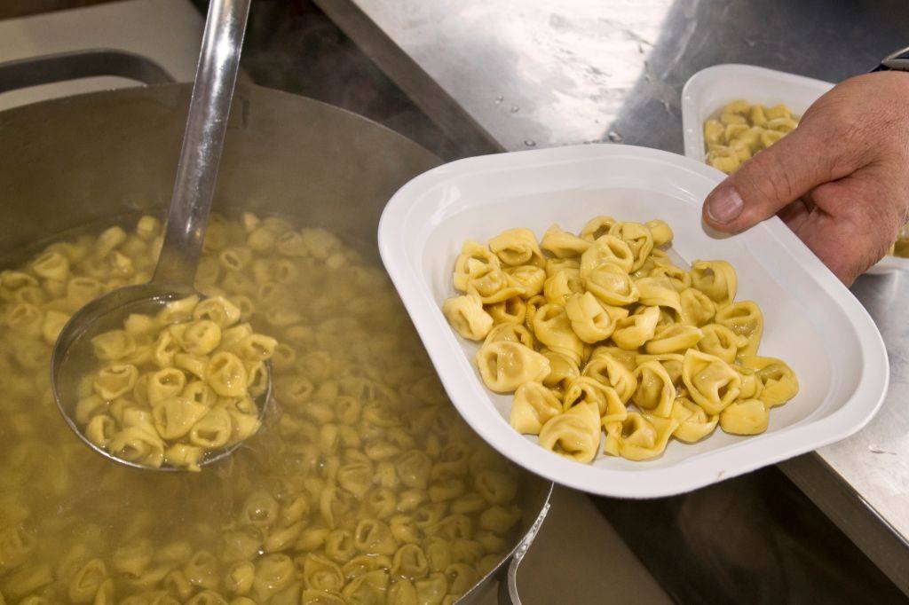 someone scooping tortellini into a bowl