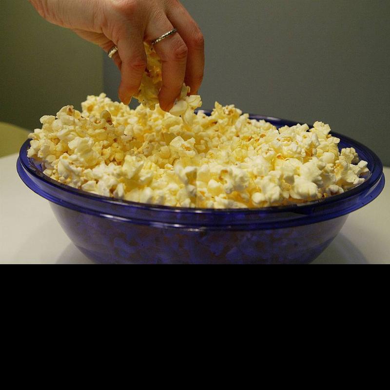 A woman grabs freshly popped microwave popcorn from a bowl