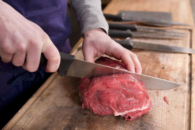 Close up shot of the hands of a butcher cutting a piece of meat.