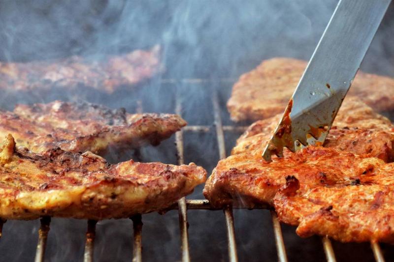 Steaks lie on a charcoal grill in a garden
