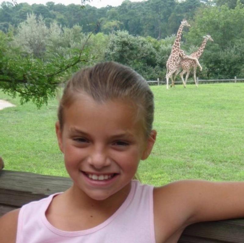 giraffes  mating in background of photo of girl at zoo