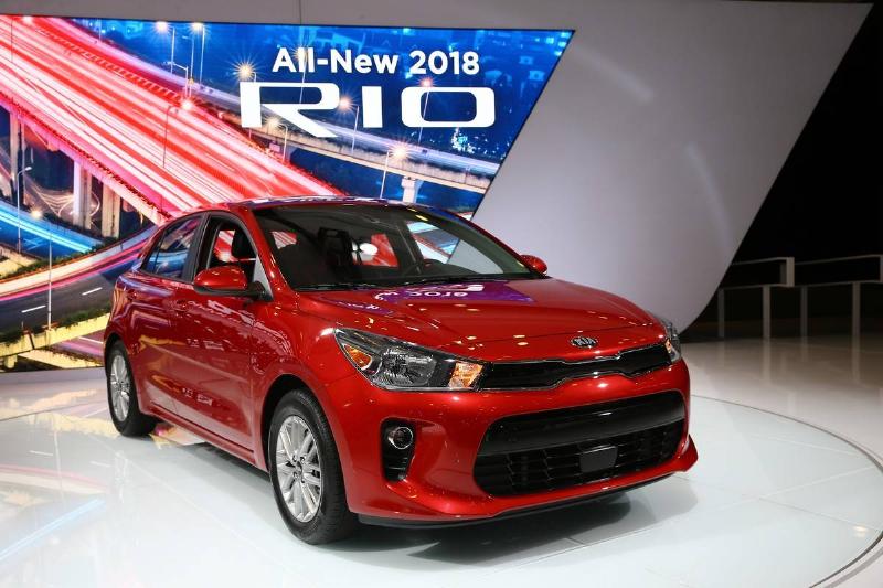 A 2018 Kia Rio is displayed beneath a sign.