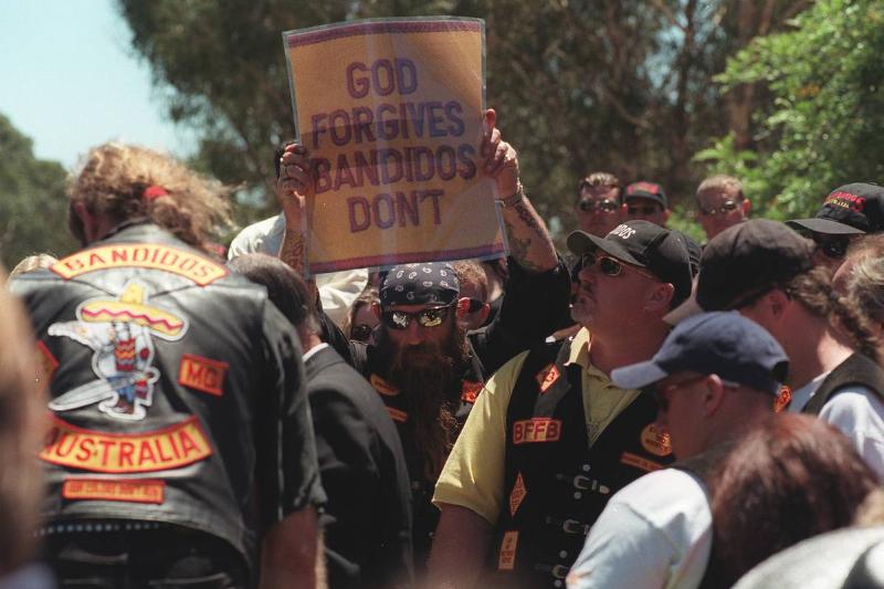 A member of the Bandidos motorcycle club holds up a sign that says, 