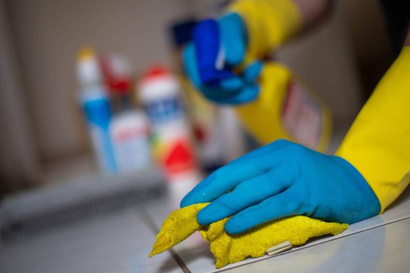person wearing rubber gloves using yellow rag to clean tile