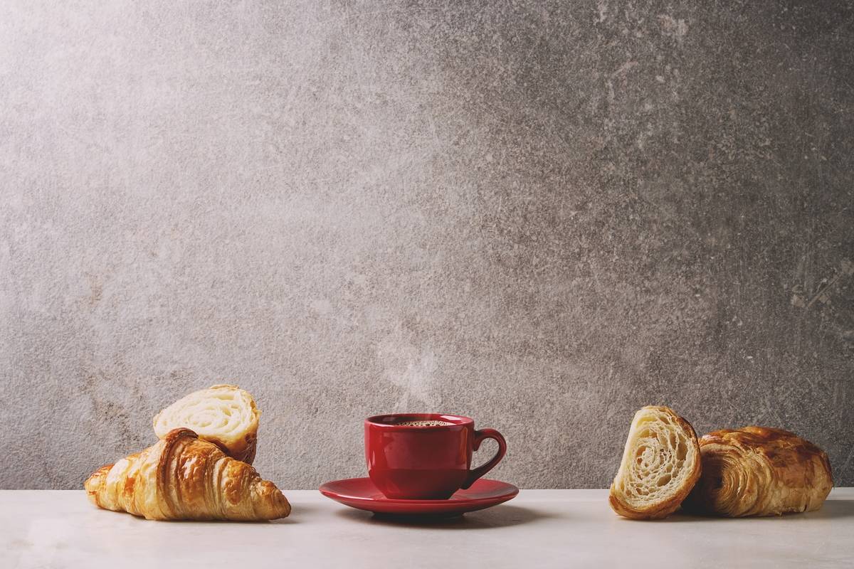 A red mug of coffee sits next to croissants.