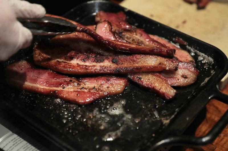 A person cooks bacon on a stove.