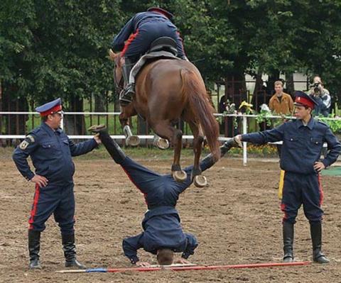 Horse jumping over a man doing the splits while upside down--it looks like the horse might hit him in the family jewels