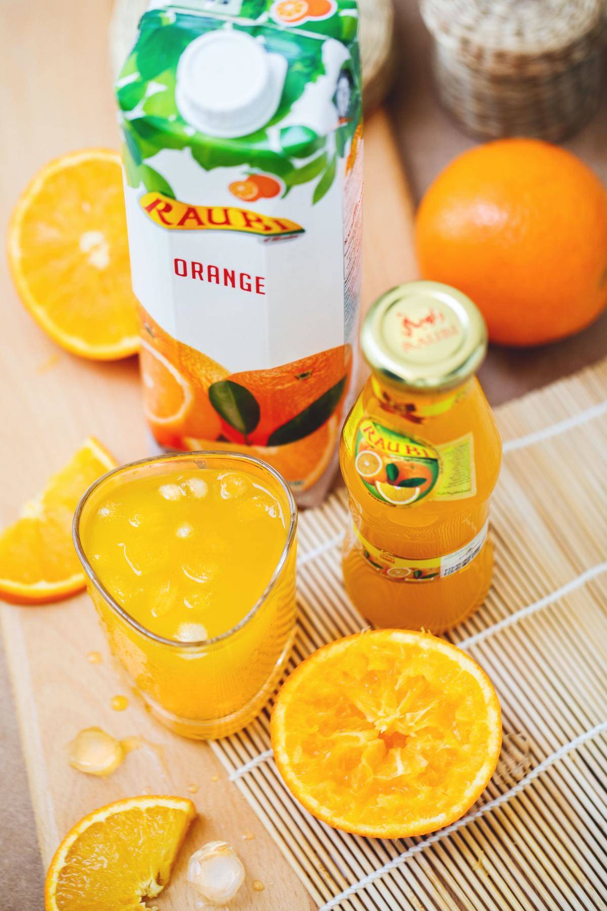 Orange juice is seen bottled and in a glass.