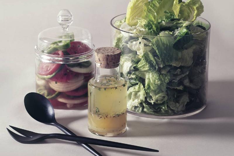 A bowl of salad leaves are seen with salad dressing and pickled vegetables.