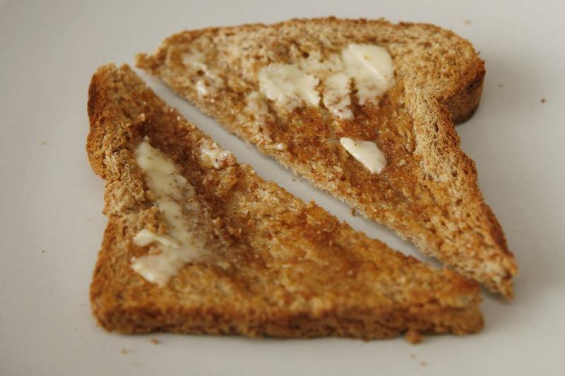 Two slices of whole grain toast have butter.