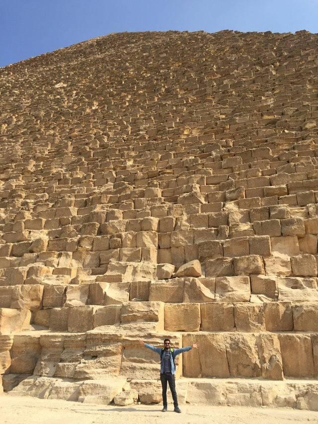 man standing at the bottom of The Great Pyramid of Giza with his arms streched outwards