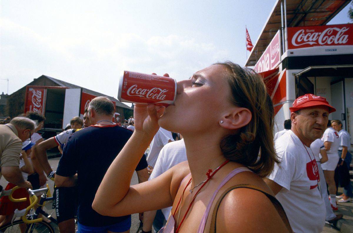 A woman drinks from a Coca-Cola can.